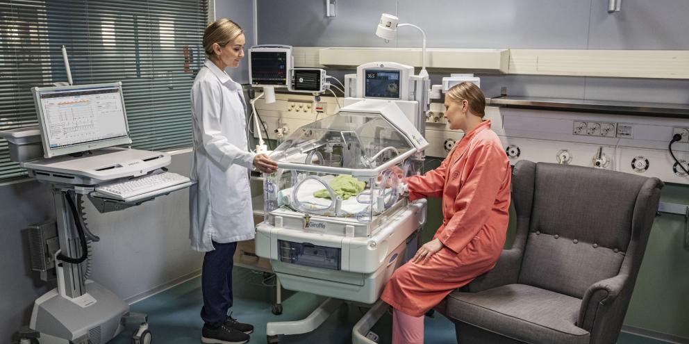 NICU patient in an incubator with a clinician and the mother's baby next to the patient