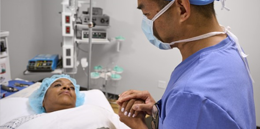 A physician holds hands with their patient