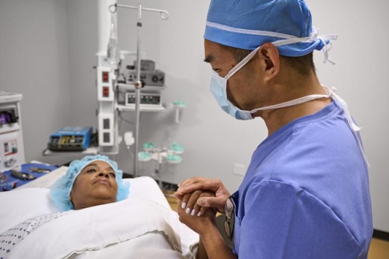 A physician holds hands with their patient