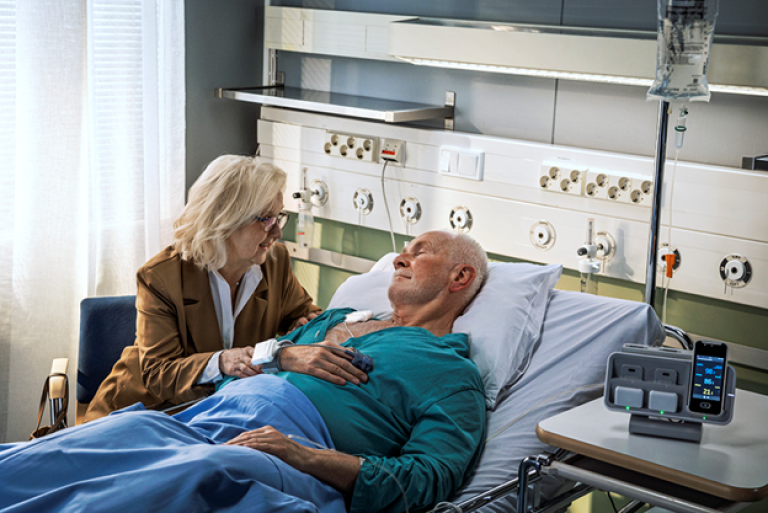 Patient laying on a bed wearing Portrait Mobile with his wife